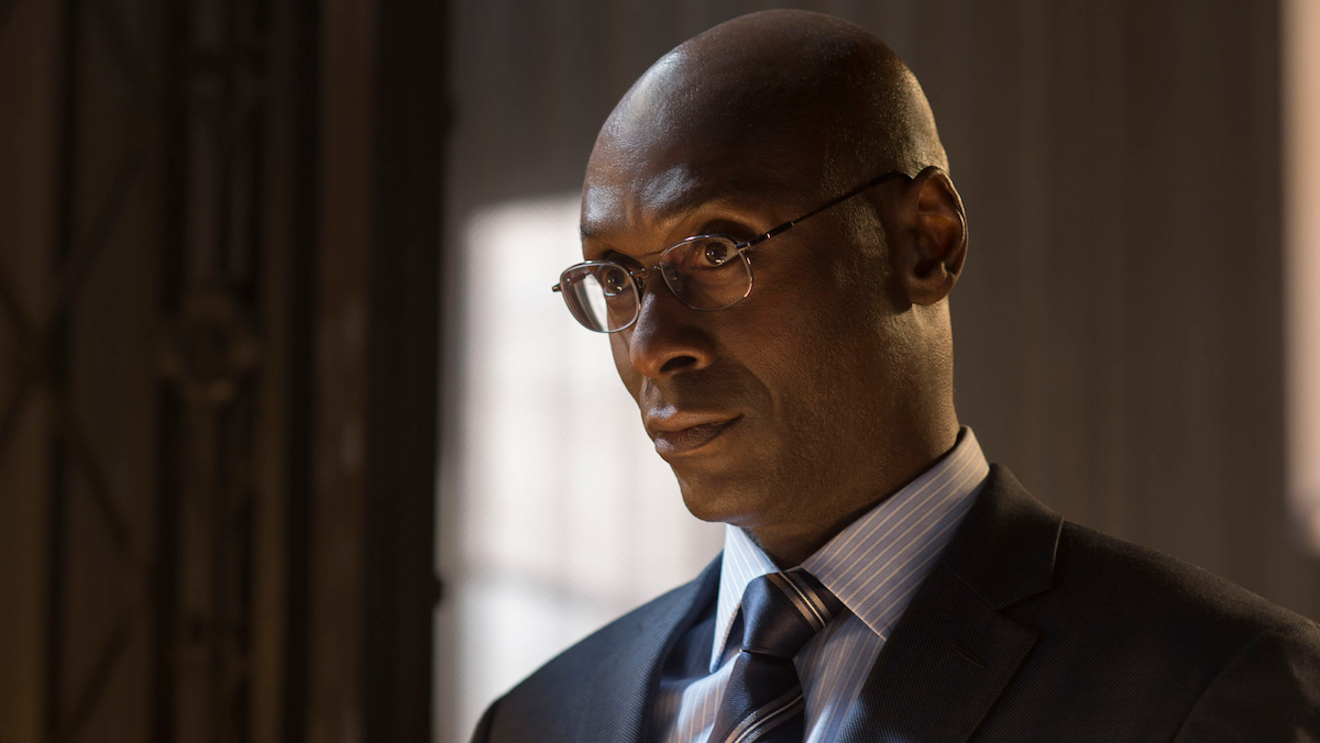 A bald man with glasses wearing a suit with a tie, Lance Reddick as John Wick