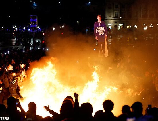 A protester holds a cut-out depicting French President Emmanuel Macron near a fire during a demonstration on Place de la Concorde on March 17, 2023