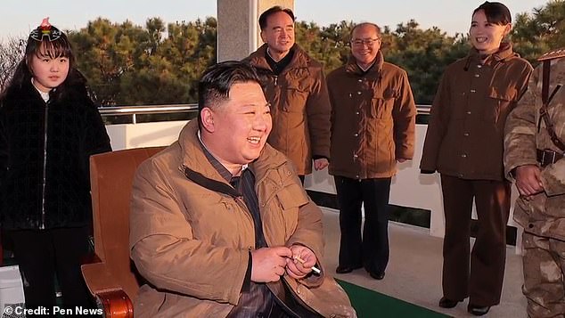 Kim Jong Un holding a cigarette in Pyongyang, North Korea, surrounded by military officials and his daughter (left)