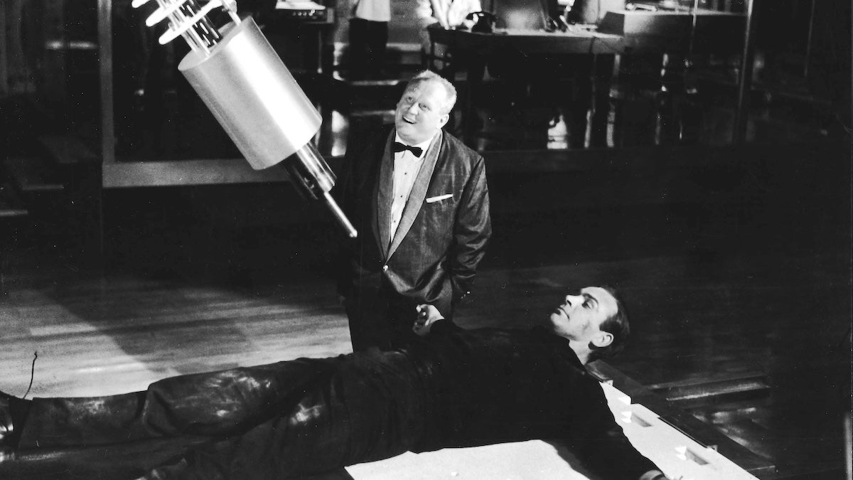 Villain Auric Goldfinger (Gert Frobe) laughs as British agent James Bond (Sean Connery) lies strapped to a table beneath a laser weapon in a still from the film "Goldfinger."
