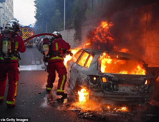 Firefighters work to put out a burning car on the sidelines of a demonstration in Nanterre