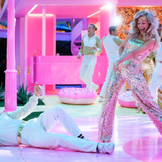 In the middle of a disco dance sequence in "Barbie," Barbie (Margot Robbie) in a sparkling jumpsuit points down to the floor at Ken (Ryan Gosling), who is lying down looking up at her and giving her a thumbs up.