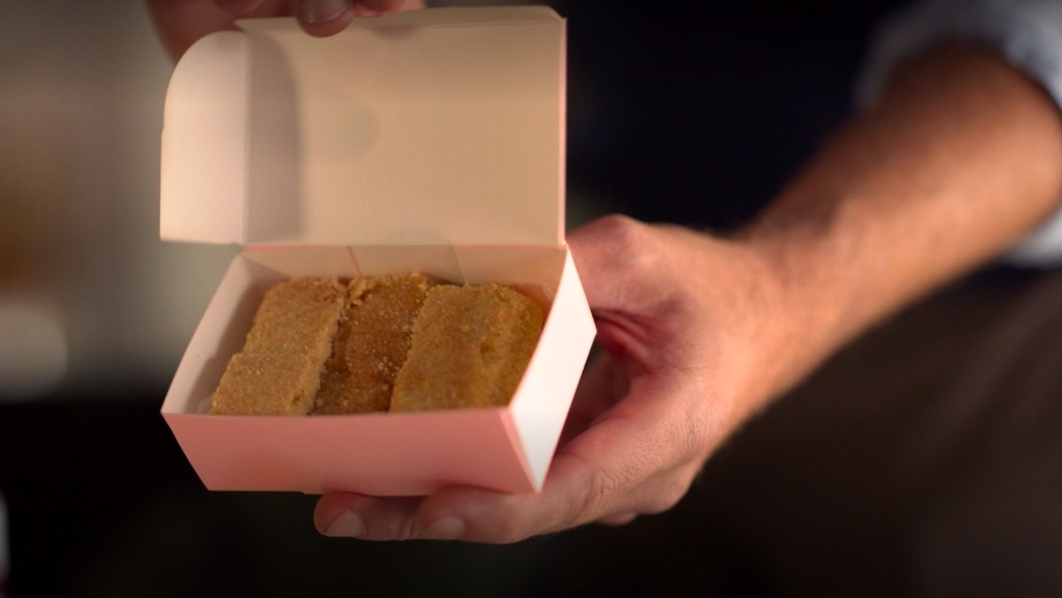 A small pink box of shorttbread biscuits being held by Ted Lasso