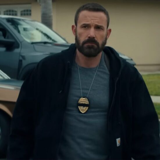 Ben Affleck in a tee and jacket and wearing a cop badge outside of a home in The Rip.
