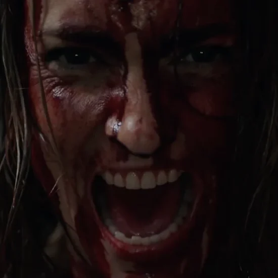 Closeup of a woman covered in blood screaming at the camera.