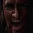 Closeup of a woman covered in blood screaming at the camera.