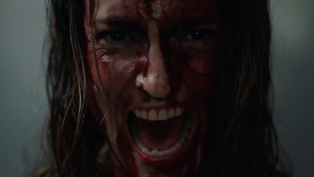 Closeup of a woman covered in blood screaming at the camera.