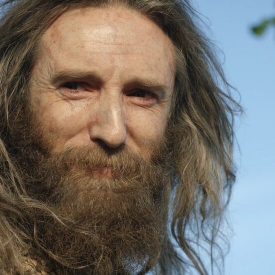 Daniel Weyman as the Stranger smiles in the sun on The Rings of Power