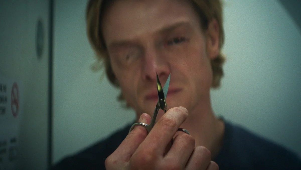 Tom Rhys Harries with goopy eyes holds up tiny scissors.