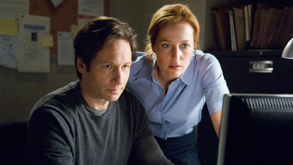 Mulder (David Duchovny) and Scully (Gillian Anderson) look at a computer screen.