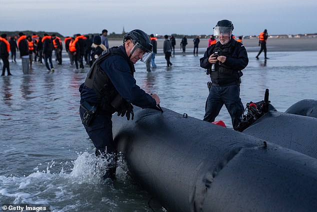 A French officer punctures an inflatable vessel with a knife after it was abandoned on a beach at Gravelines, northern France, following a failed crossing attempt