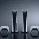 Two PlayStation 5 consoles and two DualSense controllers against a dark grey background.