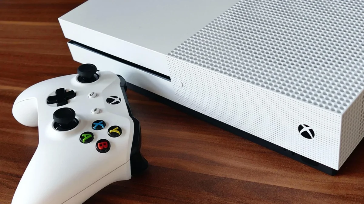 A white Xbox console and wireless controller on a wooden surface.