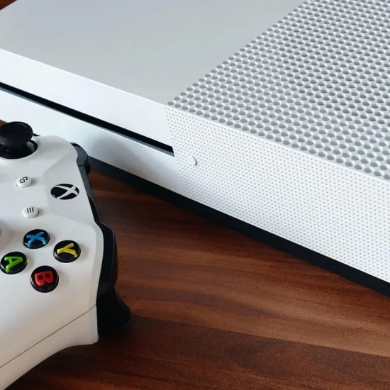 A white Xbox console and wireless controller on a wooden surface.
